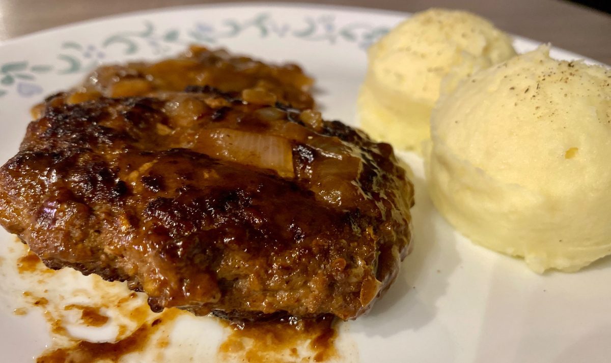 Steak haché aux oignons servi avec des patates pilées dans une assiette